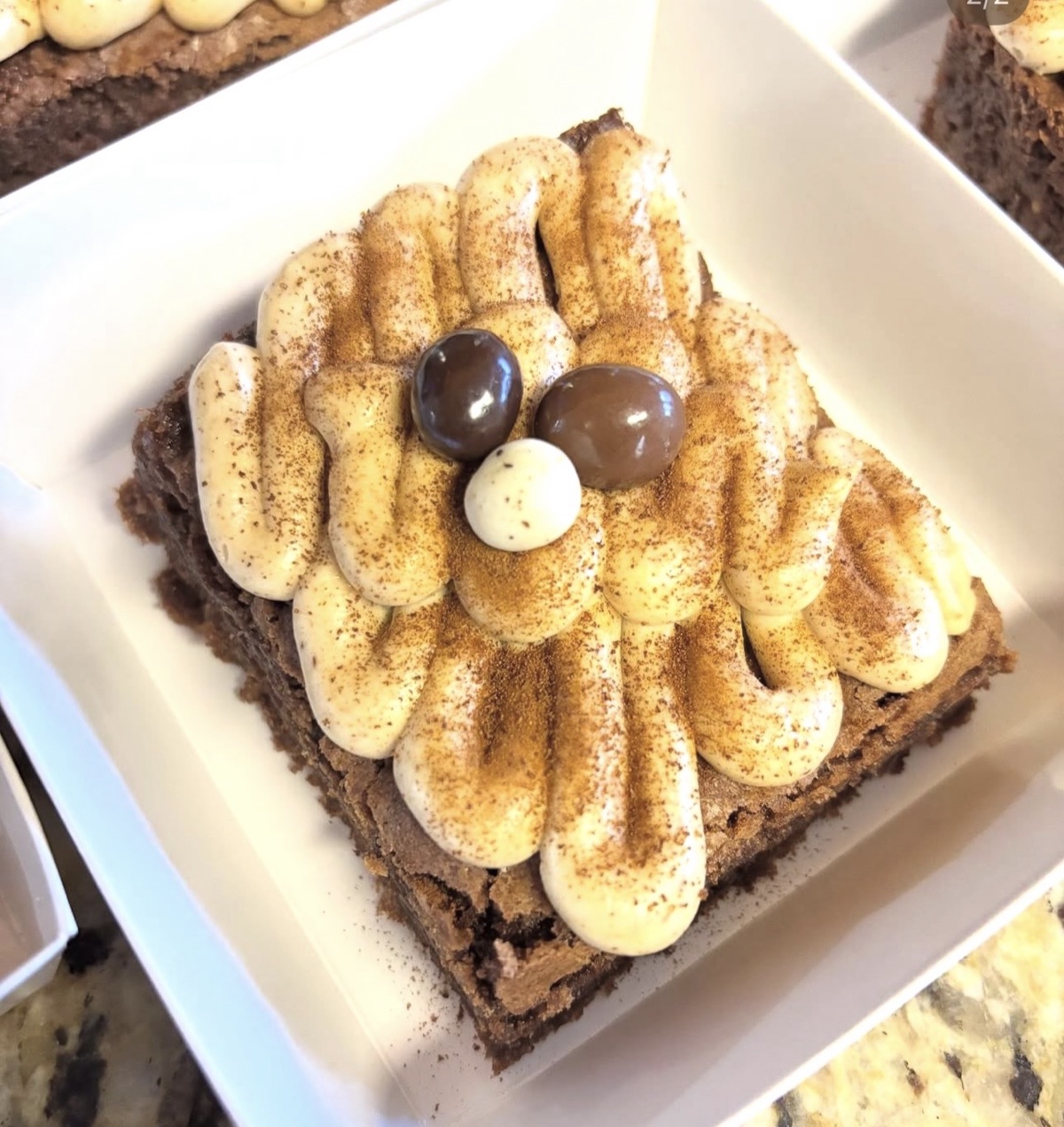Freshly finished brownie topped with vanilla cream, chocolate pieces, and cinnamon